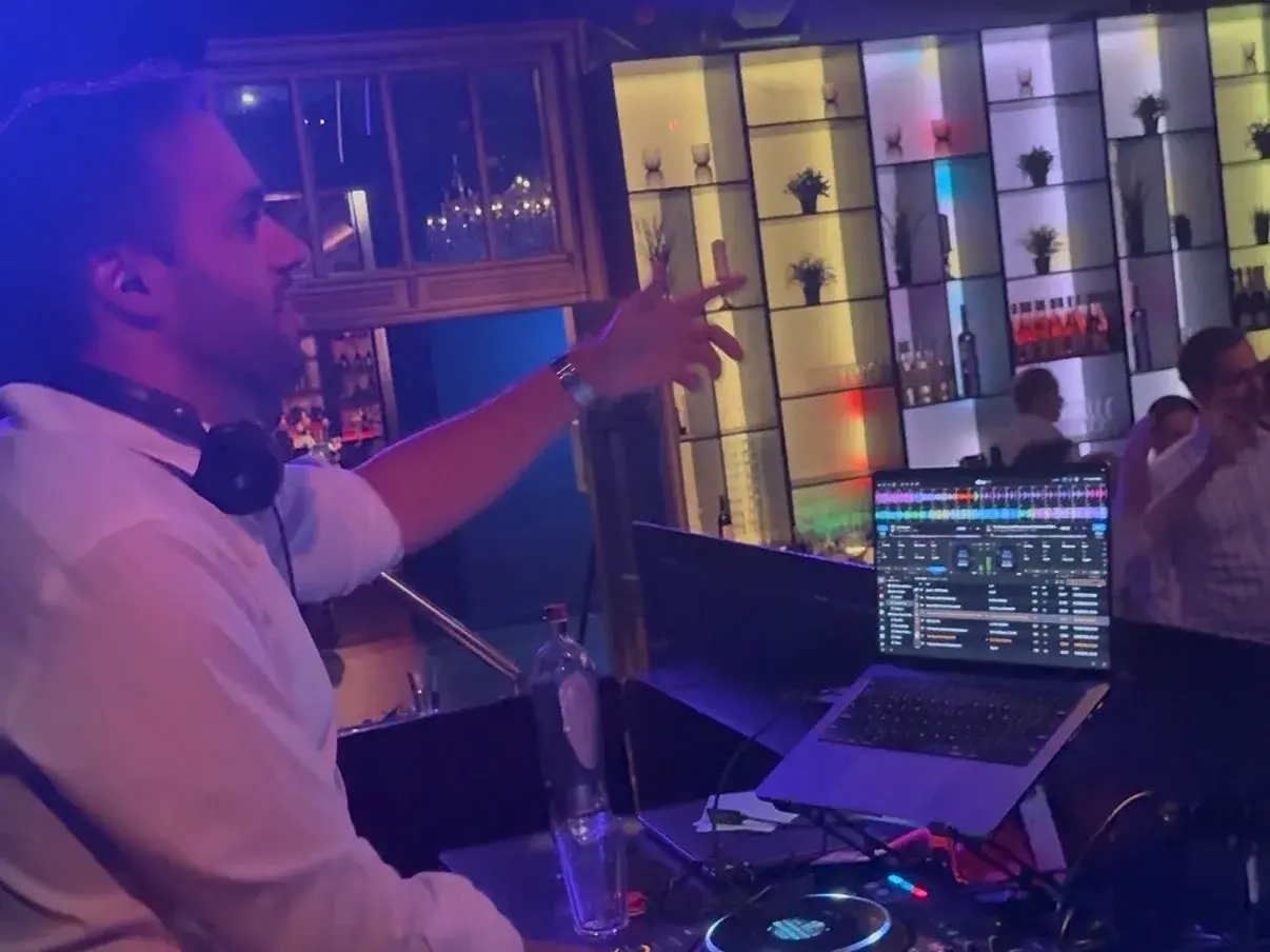 DJ Mathix achter de decks in een club met discoballen, één arm in de lucht