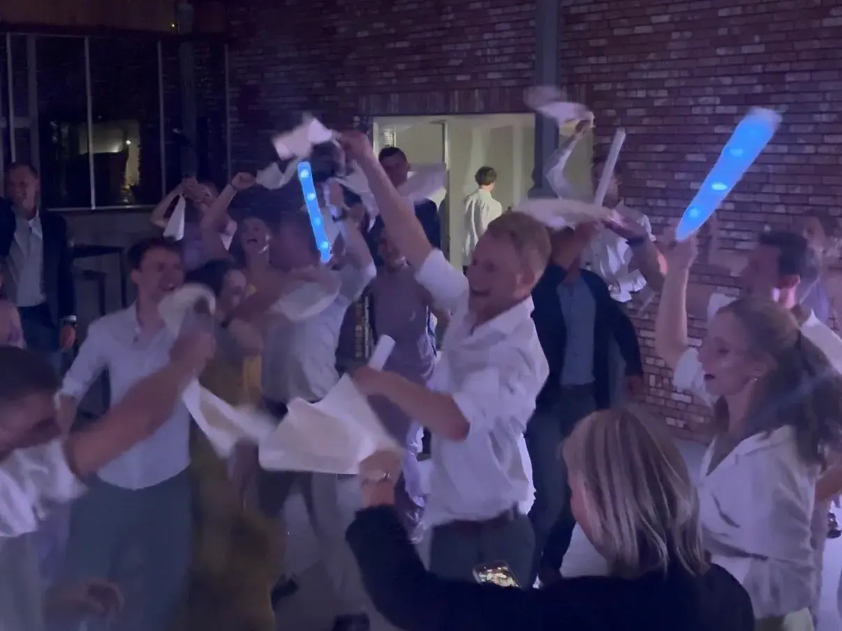 Gasten zwaaien met servetten en lichtstaven op een trouwfeest onder witte doeken